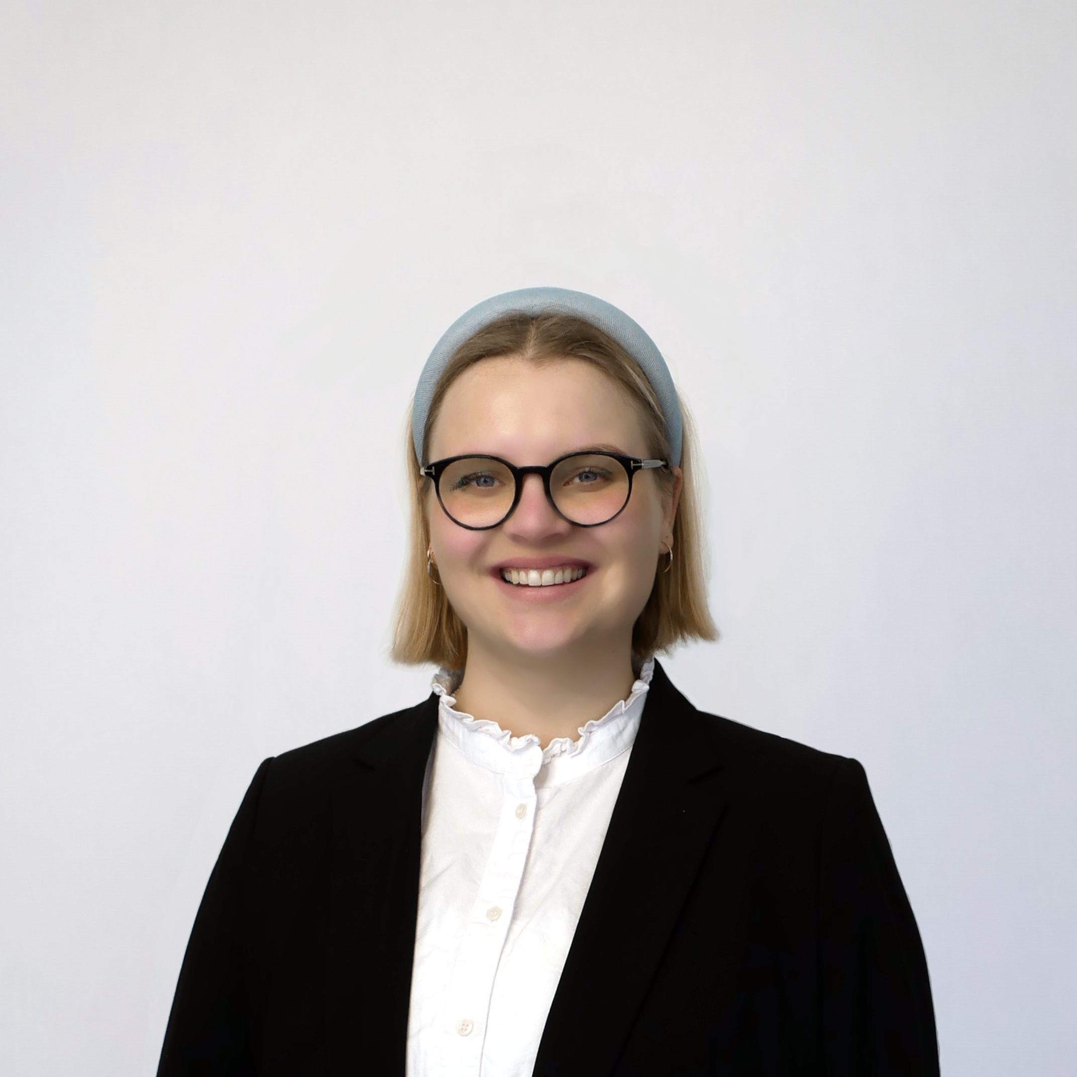 Frau Krüger ist ab etwa dem oberen Brustkorb abgebildet. Sie steht frontal zur Kamera, die Arme liegen seitlich dem Brustkorb an. Sie trägt eine weiße Bluse unter einem schwarzen Sakko. Sie trägt goldfarbene Kreolen sowie eine Brille mit runden Gläsern und schwarzem Gestell. Ihre Augenfarbe ist blau. Frau Krüger lächelt freundlich mit halboffenem Mund, sodass die obere Zahnreihe sichtbar ist. Sie trägt blonde Haare bis etwa zur Höhe des Kehlkopfes und einen hellblauen Haarreif. Der Hintergrund des Fotos ist seicht blaugrau gefärbt mit einer zur Bildmitte hin zunehmenden Aufhellung.