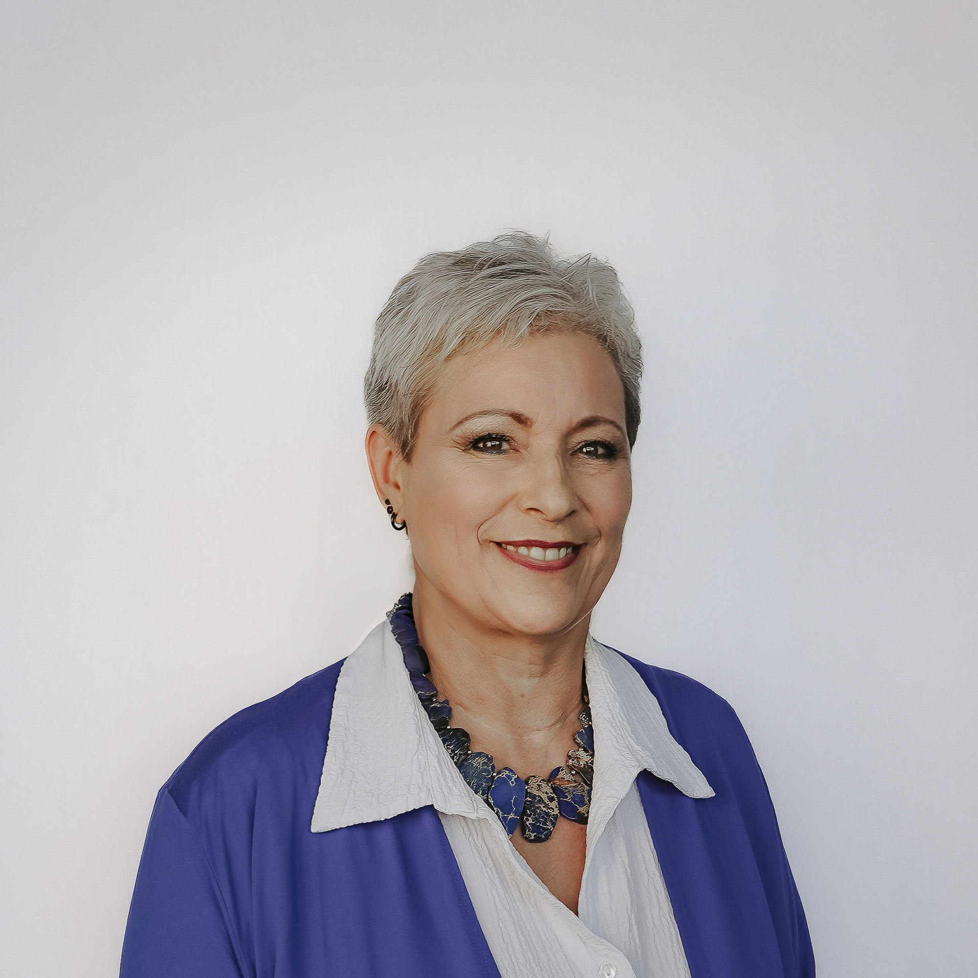 Auf diesem Bild ist Frau Berking ab etwa der Brustmitte abgebildet. Sie steht frontal und leicht zu ihrer linken Seite gedreht, die Arme hängen seitliche herab und liegen dem Rumpf an. Sie trägt eine weiße, langärmelige Bluse mit weißem Kragen und eine roayalblaue, langärmelige, offen Blusenjacke. Um den Hals trägt Frau Berking eine Halskette mit aneinander gereihten Scheiben bläulicher Edelsteine. Ihre weiß-grauen Haare trägt Frau Berking als Kurzhaarfrisur, sie hat braune Augen und lächelt freundlich in die Kamera, sodass die obere Zahnreihe zu sehen ist. Im rechten Ohrläppchen zeigen sich ein schwarzer Ohrring sowie zwei schwarze Ohrstecker. Der Hintergrund des Fotos ist seicht blaugrau gefärbt mit einer, zur Bildmitte hin zunehmenden Aufhellung.